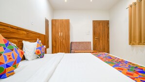 Quarto de hotel com uma cama grande, cabeceira de madeira, uma mesa pequena e duas portas.