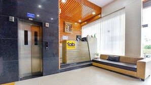 Zona de recepción de un hotel con ascensor, mostrador de recepción y sofá.