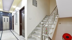 Un pasillo de hotel con piso de mármol, una escalera con barandillas metálicas y un ascensor.