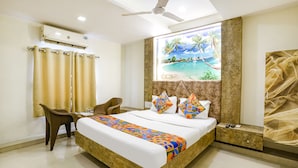 Une chambre d’hôtel équipée d’un lit, d’un bureau, d’une chaise, d’un climatiseur, d’un tableau représentant une scène de plage et d’un ventilateur de plafond.