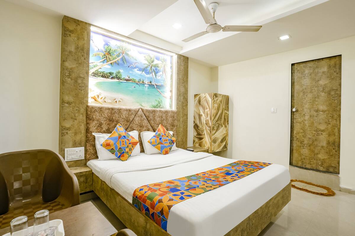A hotel room with a bed, a desk, a chair, a window with a beach view, and a ceiling fan.