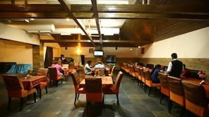A restaurant with long tables and chairs, a television screen, and a person serving. - Fabhotel Prime Chennai Deluxe (Chennai)