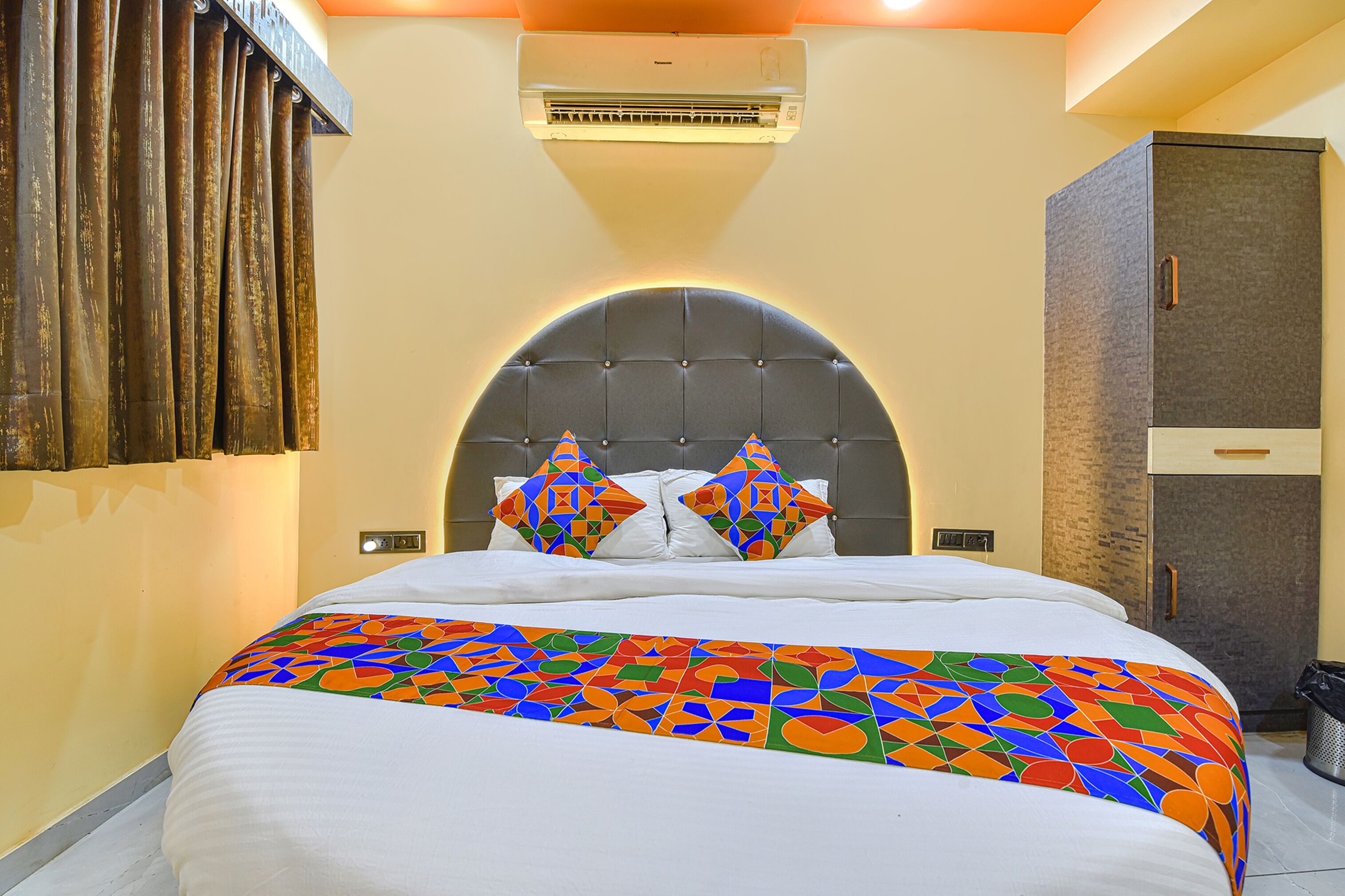 Una habitación de hotel con una cama grande, un cabecero de diseño geométrico, un equipo de aire acondicionado y un armario.
