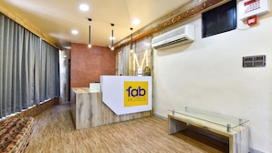 A hotel reception area with a wooden reception desk, a glass bench, and a patterned wall. - Fabhotel Max Inn (Ahmedabad)