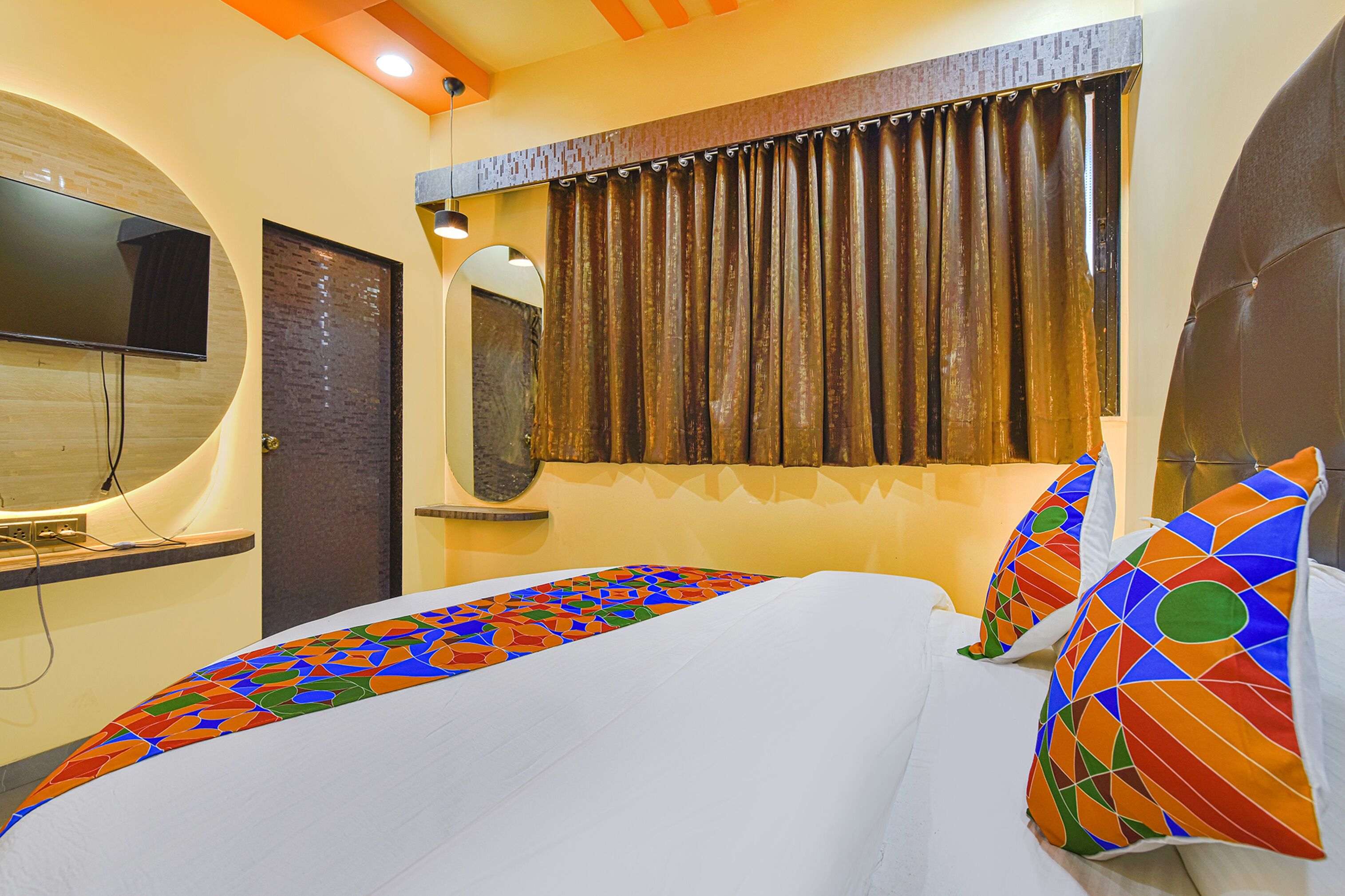 A hotel room with a large bed, a flat-screen TV mounted on the wall, and a window with curtains.
