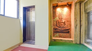 A hallway with a meditation statue, an elevator, and a green carpet. - Fabhotel Max Inn (Ahmedabad)