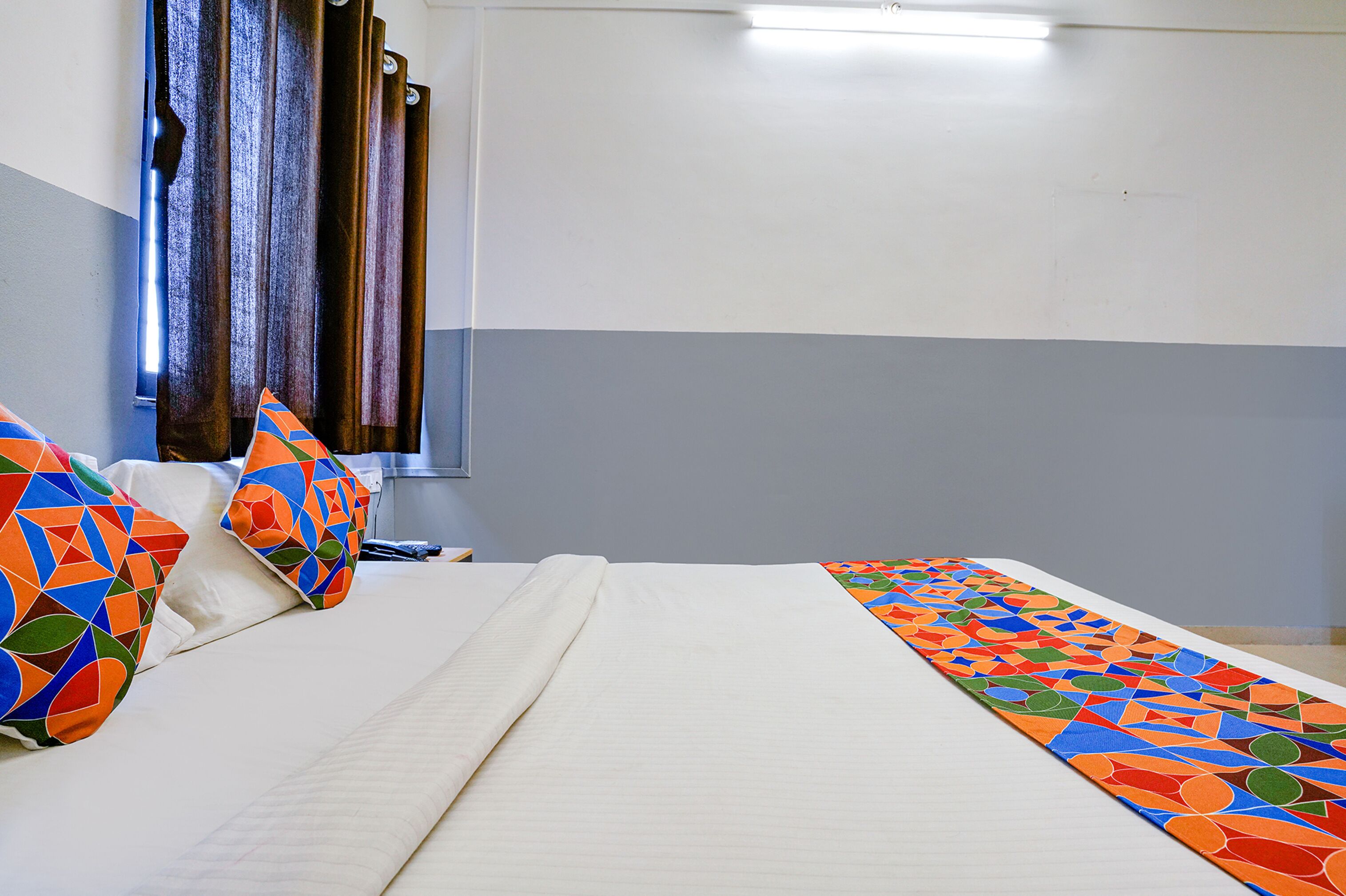 Ein Hotelzimmer mit Bett, Kissen und einer farbenfrohen Bettdecke.