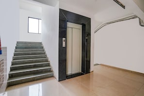 Un escalier menant à un ascenseur, dans un intérieur propre et moderne aux murs blancs et au sol carrelé.