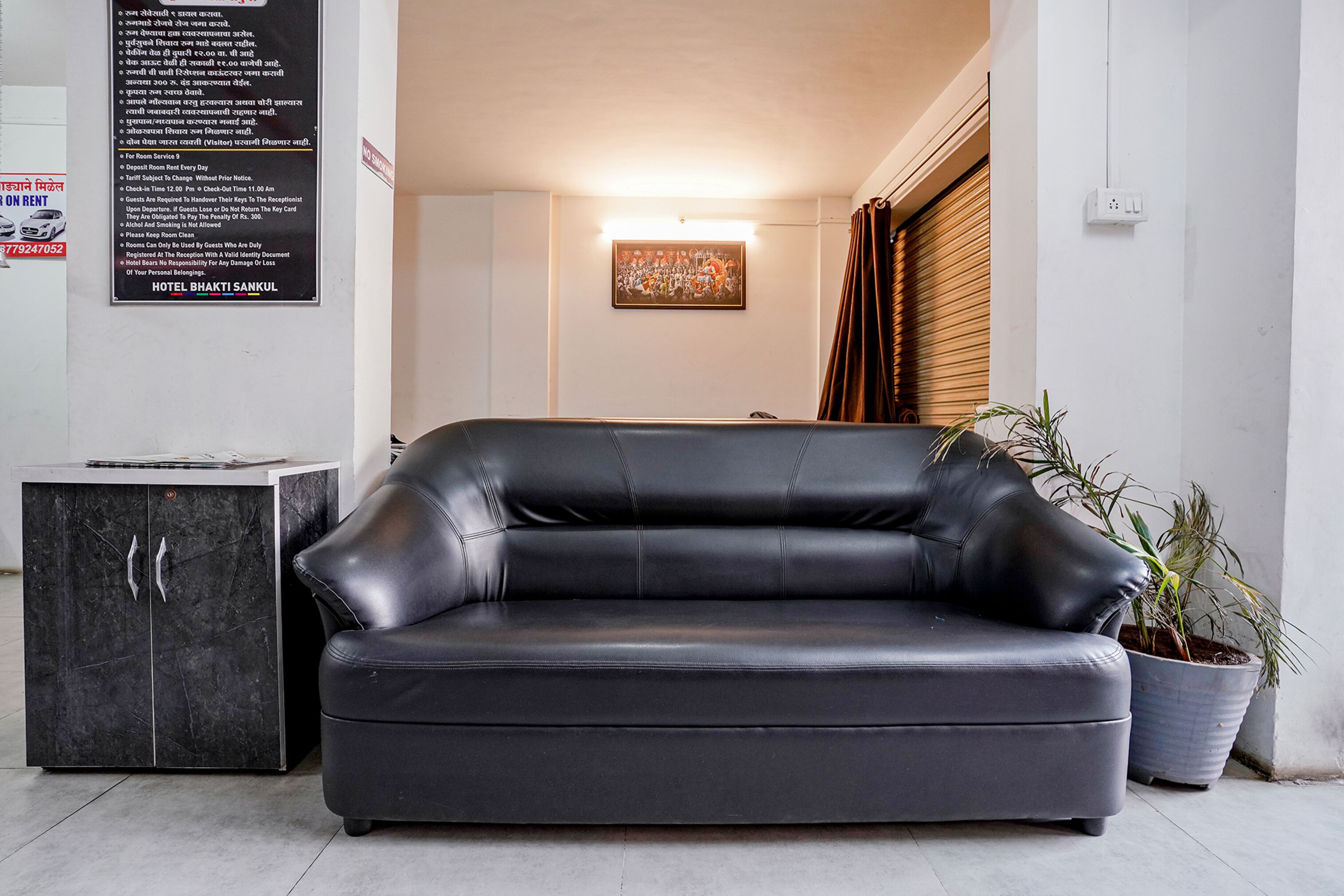 Een zwarte leren bank in een moderne kamer met een marmeren kast en een potplant.
