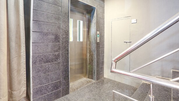 An elevator with a metallic interior and a glass door, adjacent to a staircase with metal railings. - FabHotel PP Residency (New Delhi)