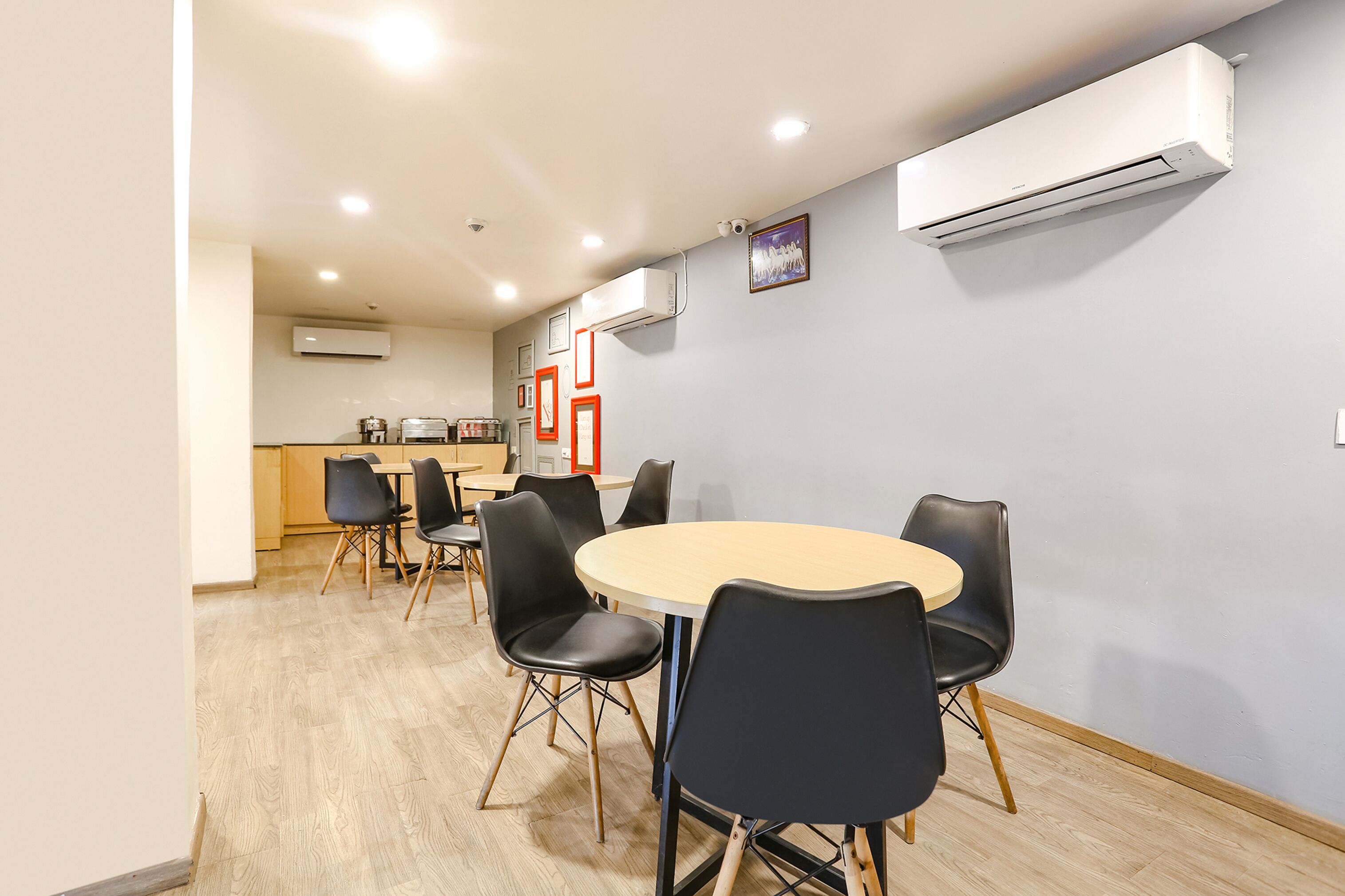 A modern dining area with a round table and black chairs, a kitchen in the background, and an air conditioning unit on the wall.