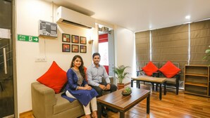 A modern hotel lobby with a sofa, a coffee table, and a seating area with red cushions. - FabHotel PP Residency (New Delhi)