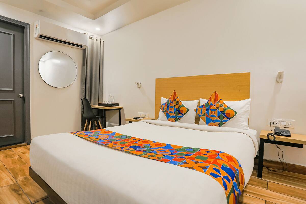 A hotel room with a bed, a desk, a chair, a round mirror, and a nightstand with a phone.