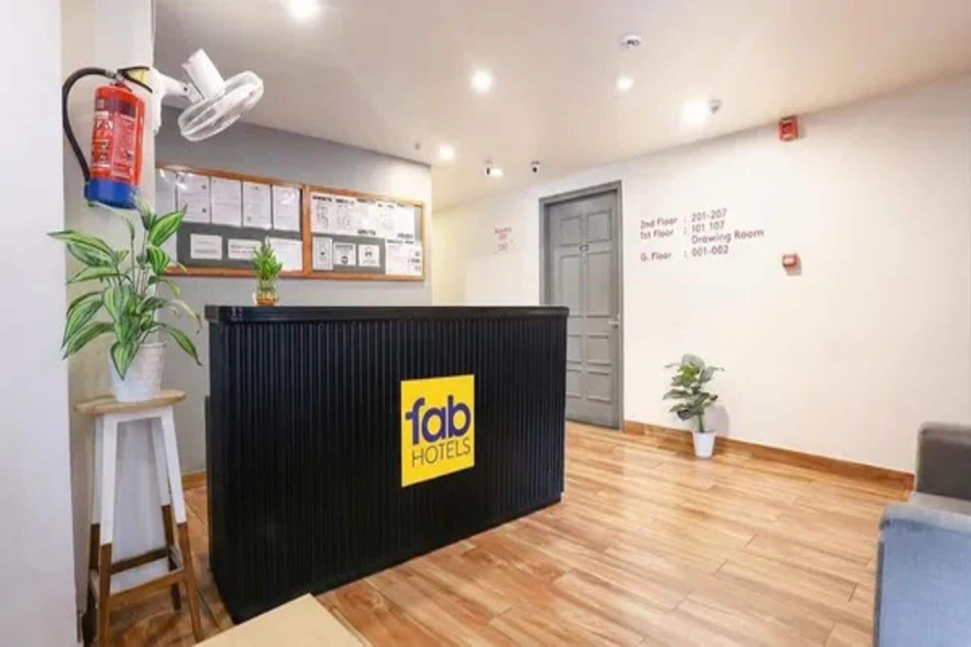A reception desk with a 'fab hotels' sign, a fire extinguisher, a bulletin board with notices, and a plant.