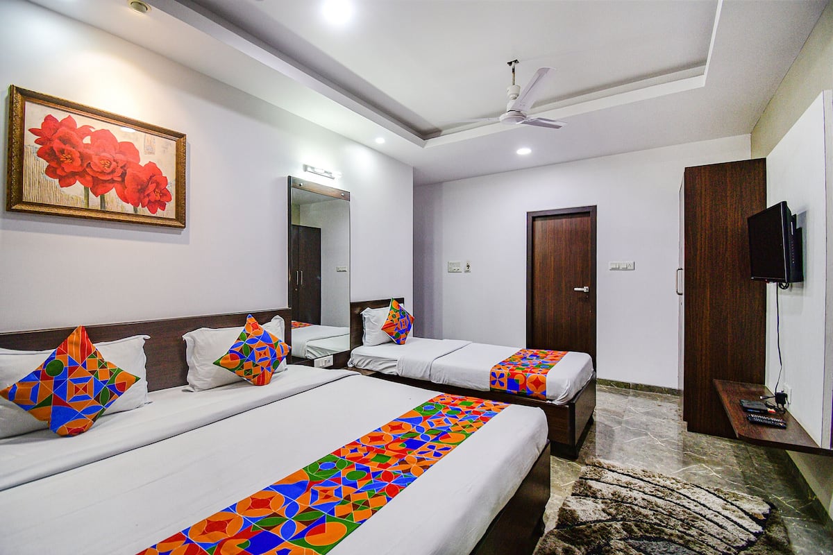 A hotel room with two beds, a ceiling fan, a TV, and a painting on the wall.