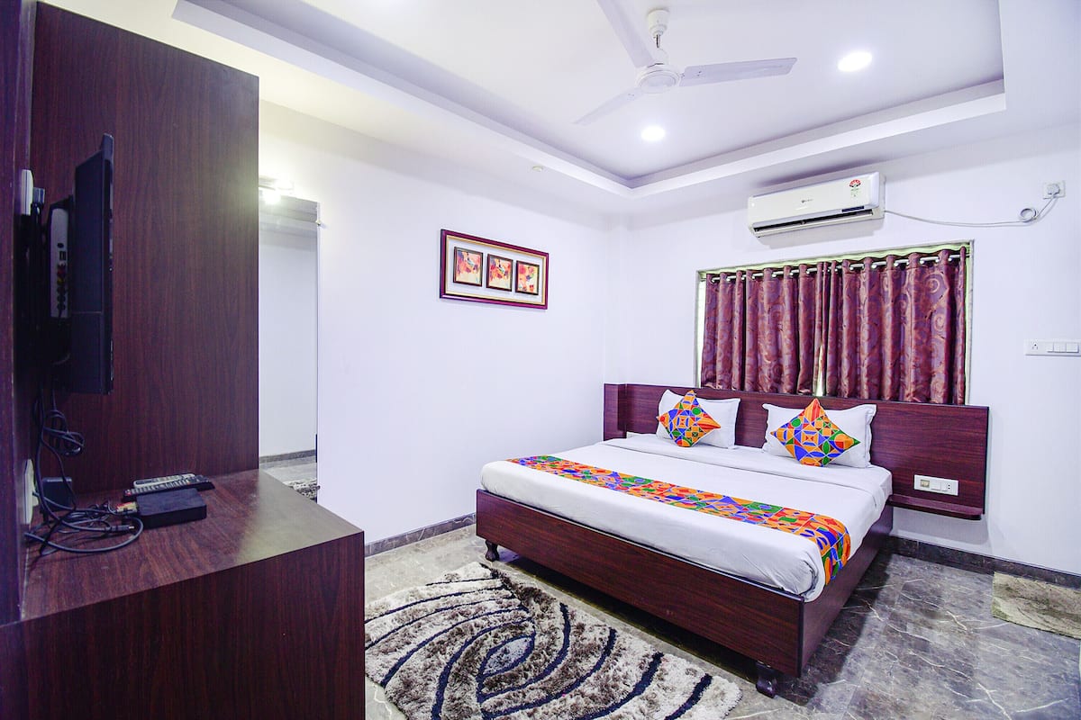 A bedroom with a bed, a TV on a stand, an air conditioner, and a ceiling fan.