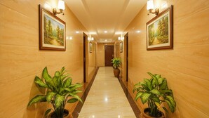 Un pasillo de hotel con paredes de madera, dos plantas en macetas, cuadros de paisajes enmarcados e iluminación empotrada.