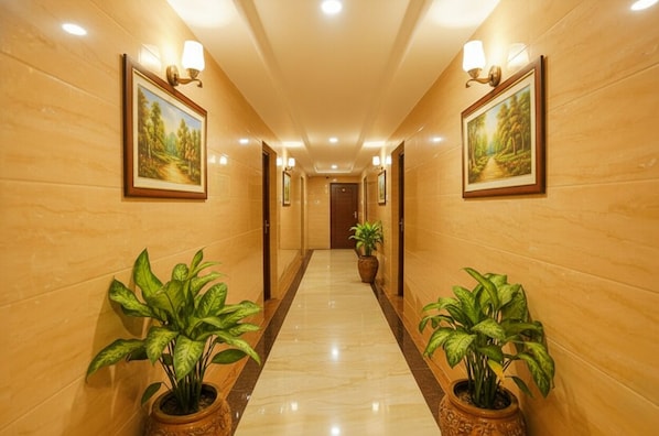 A hotel hallway with wooden walls, two potted plants, framed landscape paintings, and recessed lighting.