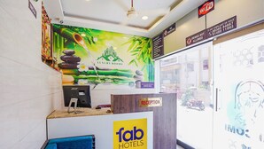 Zona de recepción de hotel con mostrador, área de descanso azul y un mural que muestra una fuente de bambú.