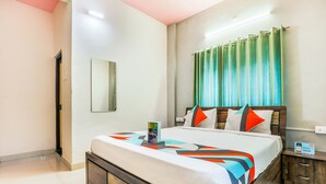 Quarto de hotel com uma cama grande, mesa de cabeceira, espelho e cortina verde.