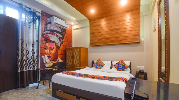 A hotel room with a bed, a wooden headboard, a nightstand, a mirror, and a wall-mounted air conditioner. - FabExpress Corinthia Boutique Rooms, Candolim Beach (Candolim)