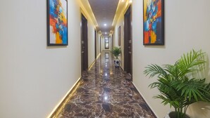 A hallway with marble flooring, framed abstract paintings on the walls, and a potted plant. - FabExpress Corinthia Boutique Rooms, Candolim Beach (Candolim)