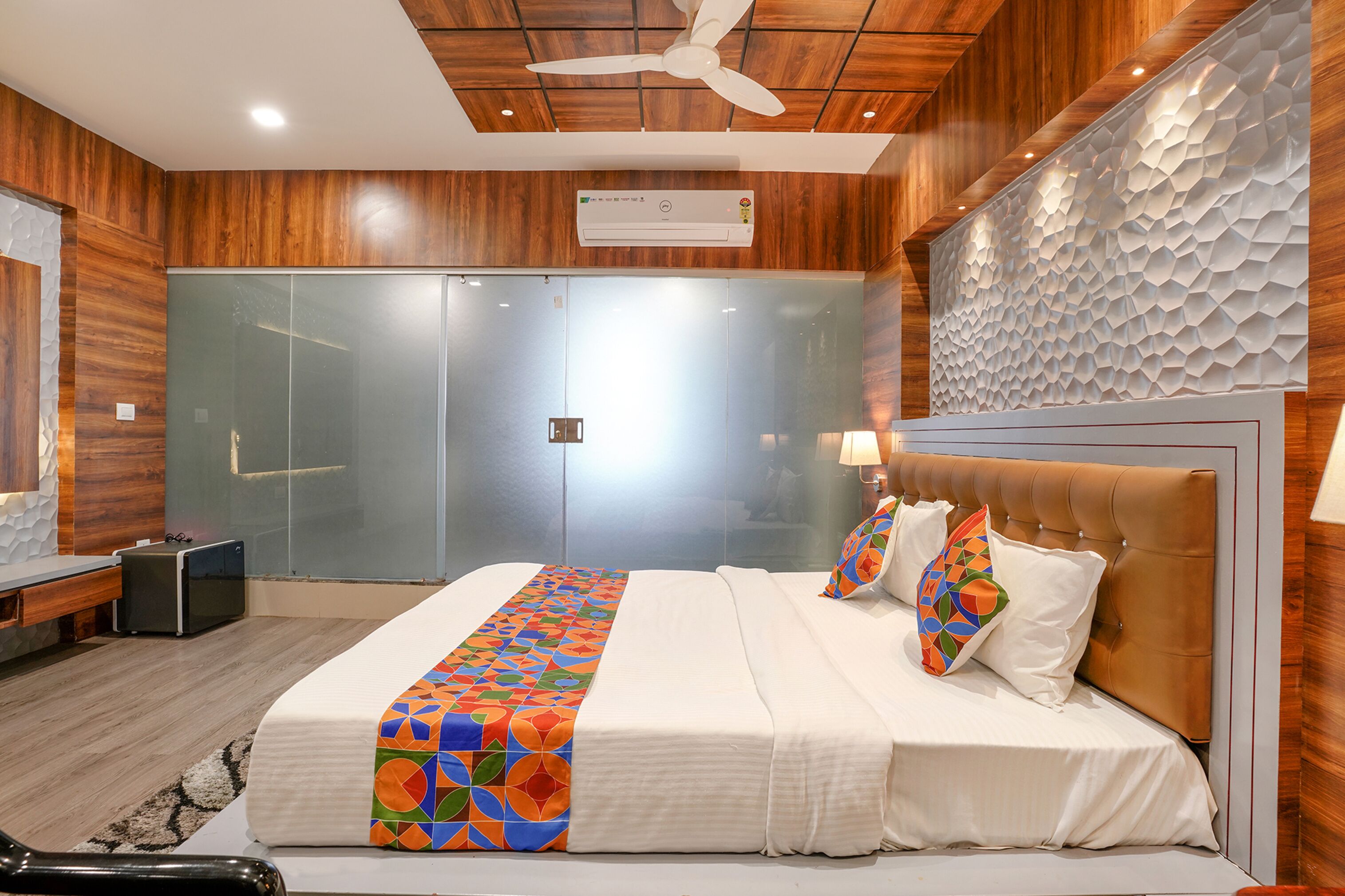 A modern hotel room with a large bed, wooden paneling, a ceiling fan, and a glass door closet.