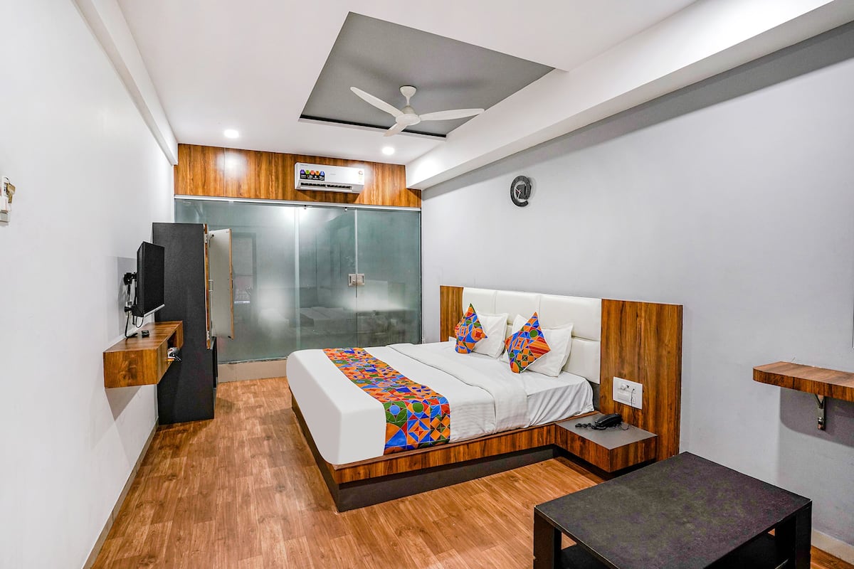A modern hotel room with a large bed, a desk, a chair, a TV, and a wardrobe.