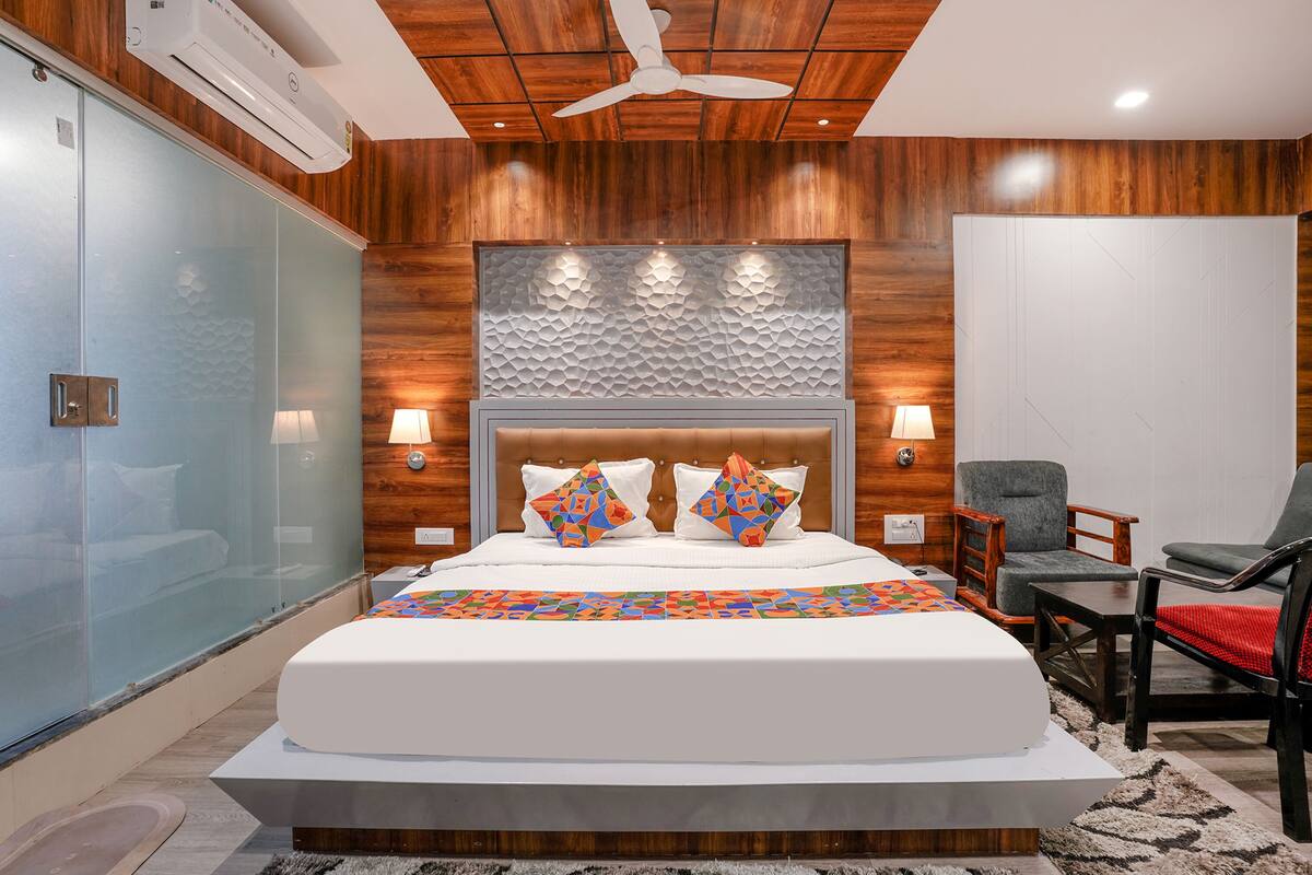 A modern hotel room with a large bed, wooden panel walls, a glass partition, and a ceiling fan.
