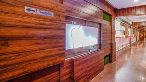 Un área de recepción con pared de madera, un cartel que indica el camino a la recepción y un gran letrero iluminado que dice "TH HOTEL".