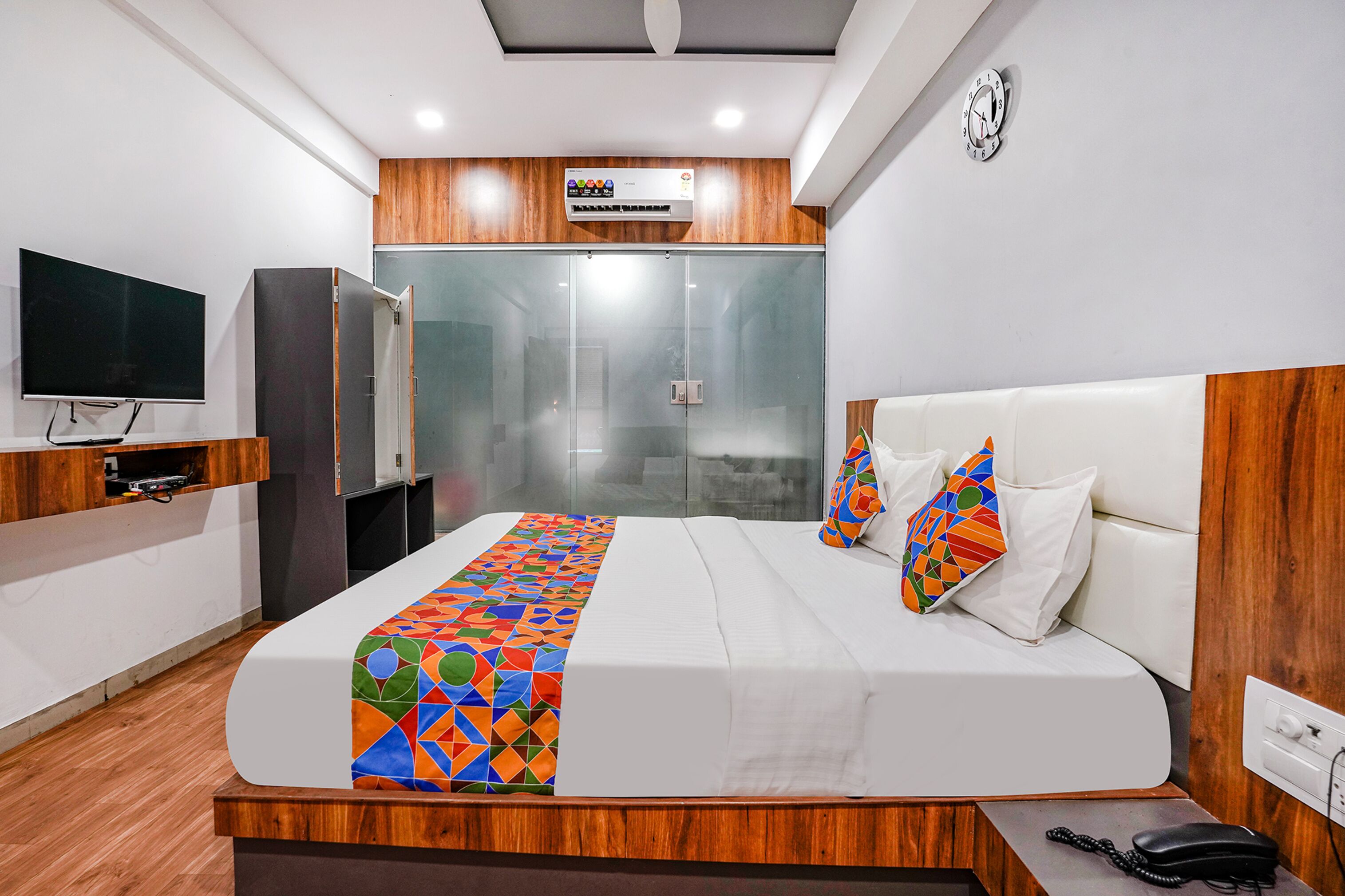 A modern hotel room with a large bed, a TV, a minibar, and a wooden headboard.