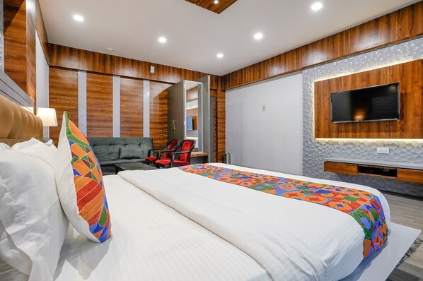 A modern hotel room with a large bed, a TV mounted on the wall, and a seating area with a chair and a table.
