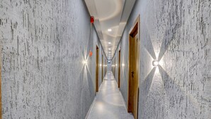 Un largo y estrecho pasillo con paredes de mármol y puertas de madera, que conduce a una habitación luminosa y bien iluminada.