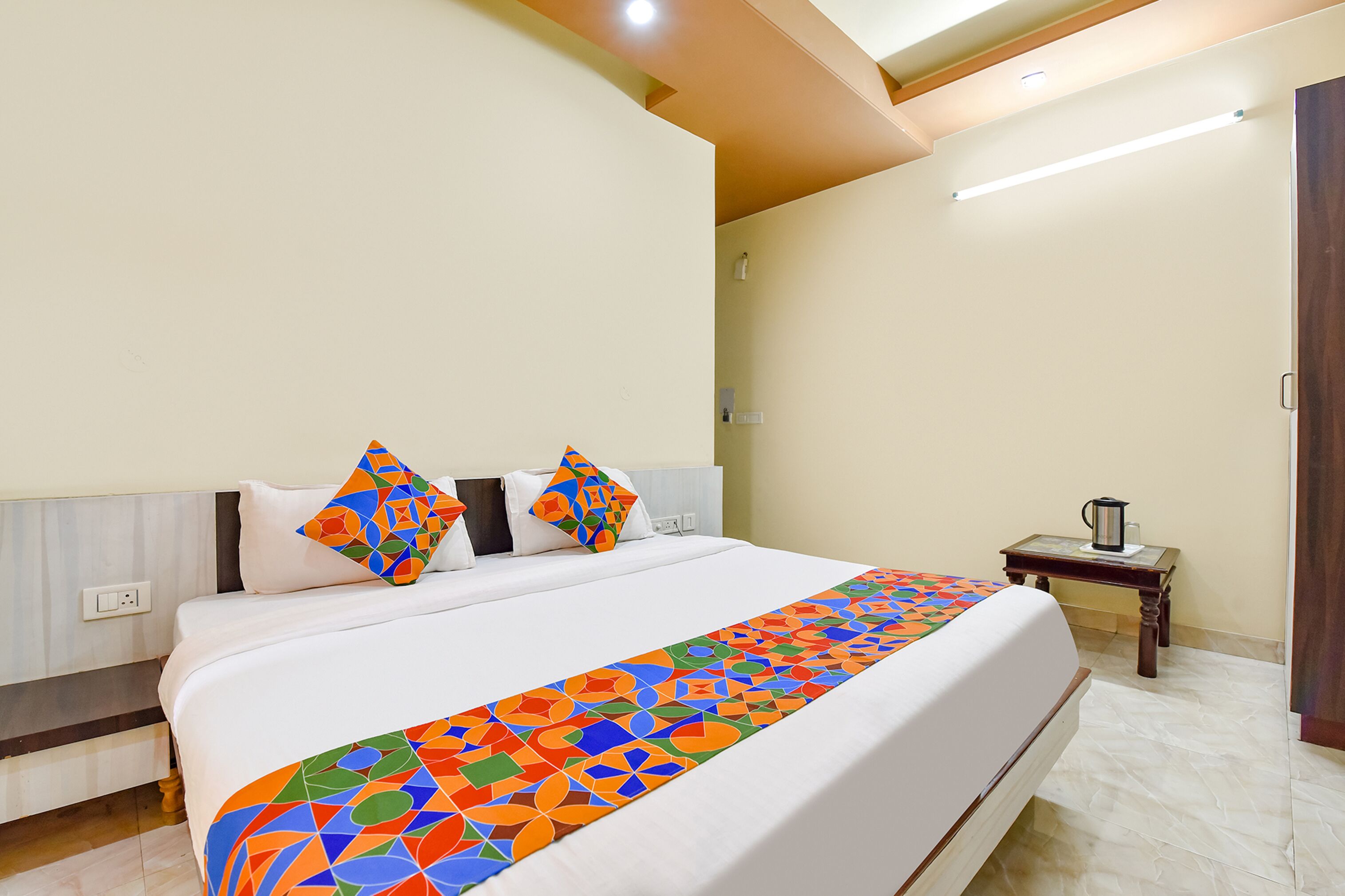 Habitación de hotel con una cama grande, una mesita de noche con lámpara y una puerta de madera.