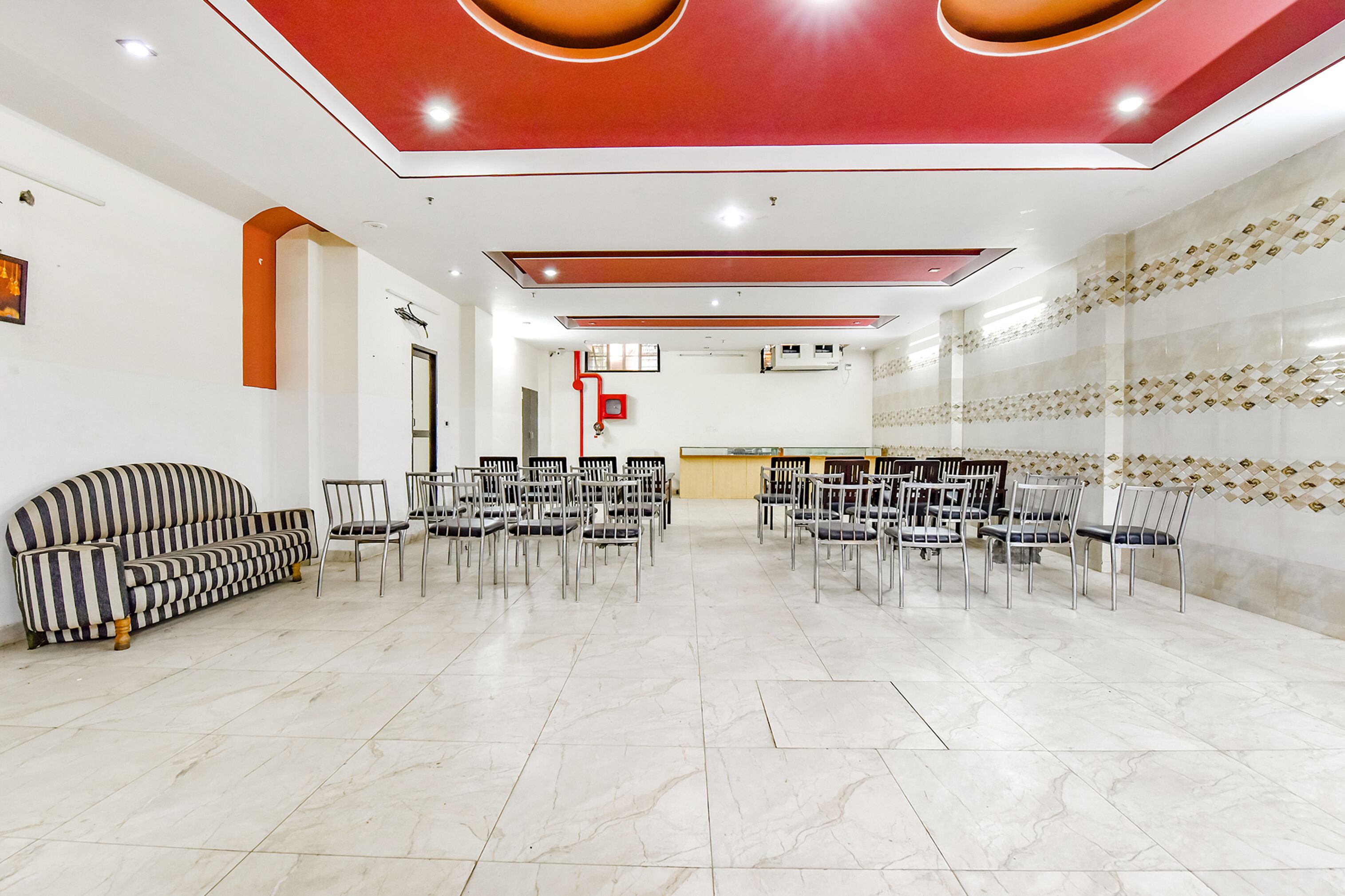Un vestíbulo amplio con un sofá a rayas, múltiples sillas dispuestas para sentarse, un mostrador de recepción y una pared decorativa con un diseño geométrico.