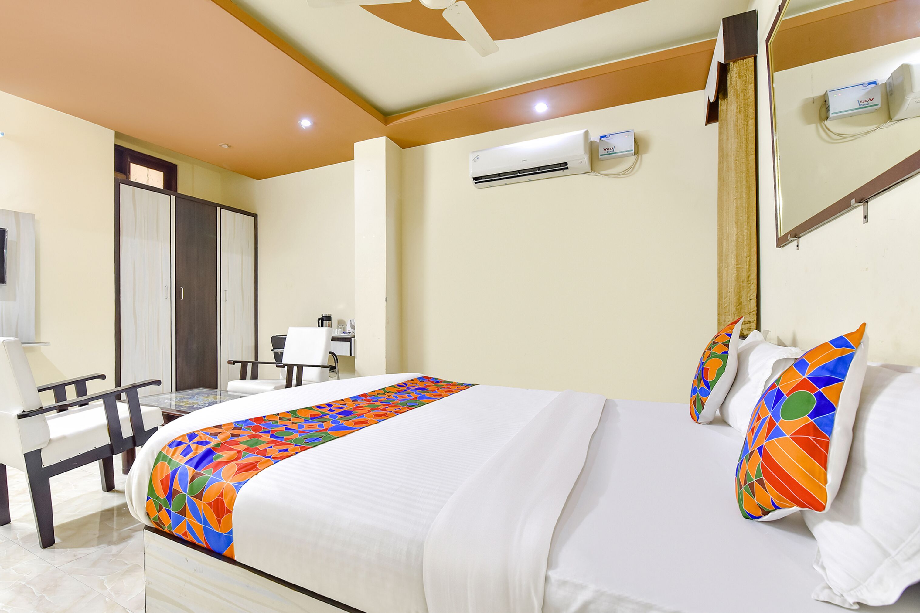 Habitación de hotel con cama, escritorio, silla, equipo de aire acondicionado y espejo.