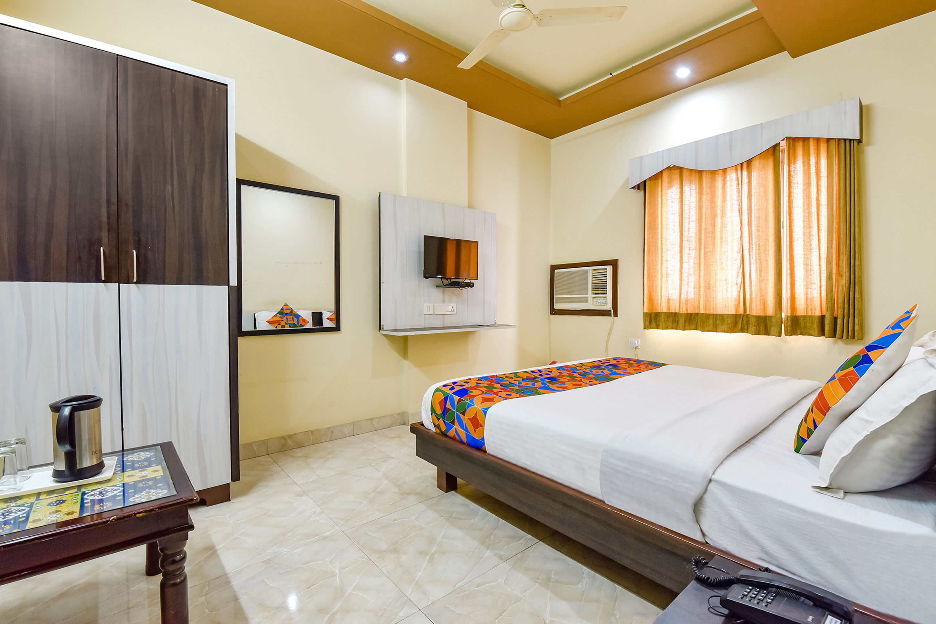 A hotel room with a bed, a wardrobe, a television, and a window with curtains.