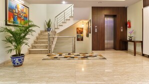 Un vestíbulo moderno con suelo de mármol, una escalera, una puerta de madera y un extintor.