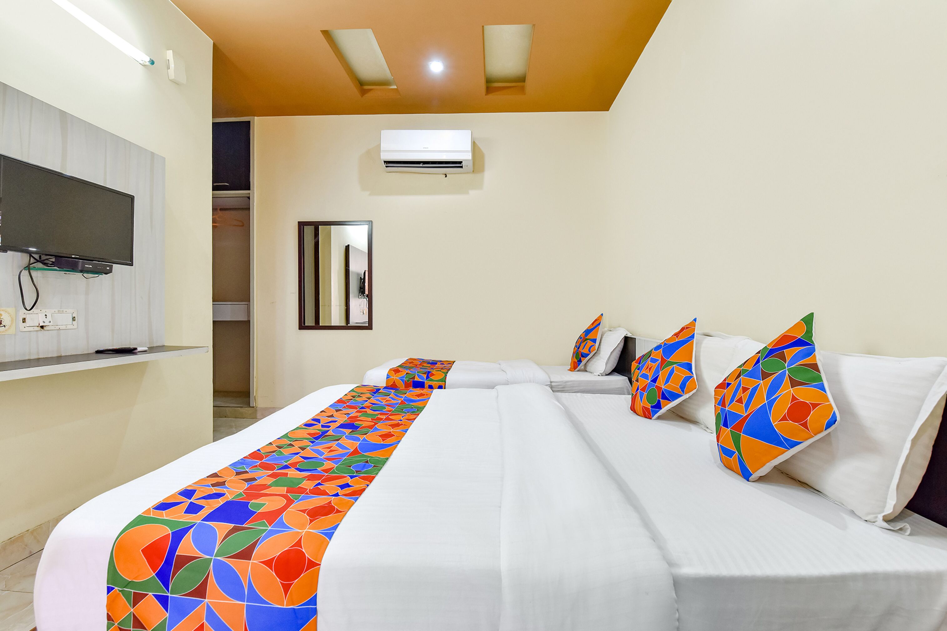 Een hotelkamer met een groot bed, een aan de muur bevestigde televisie, een airconditioner en een spiegel.