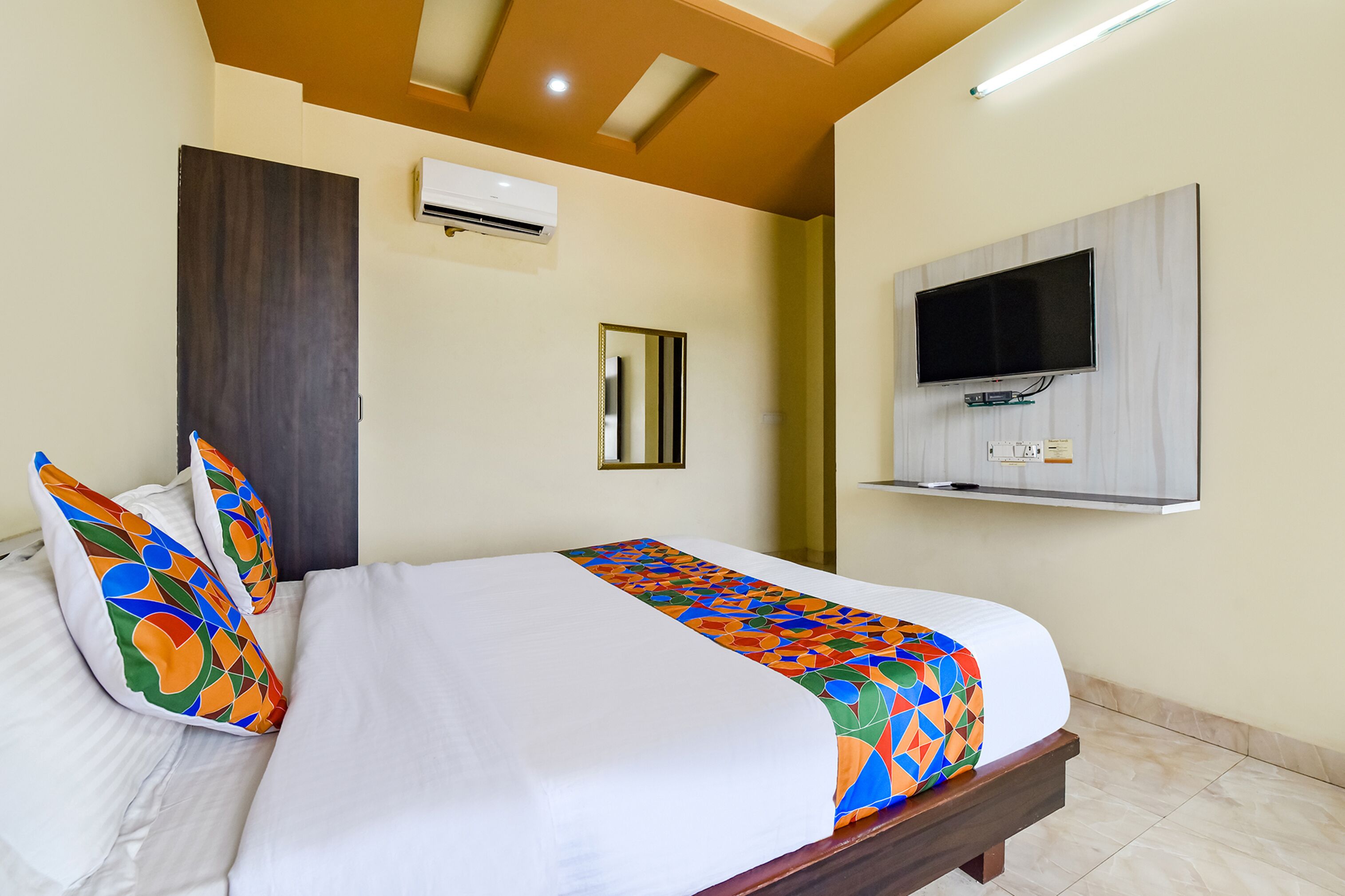 A hotel room with a bed, a TV mounted on the wall, and an air conditioning unit.