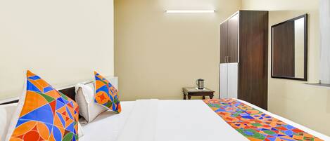 A hotel room with a large bed, a bedside table with a kettle, and a mirror on the wall.