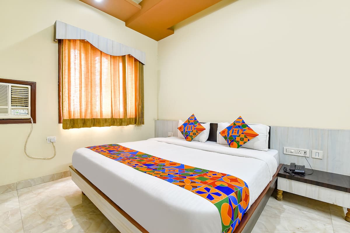 A neatly made bed with a colorful geometric-patterned bedspread, a bedside table with a phone, and a window with curtains.