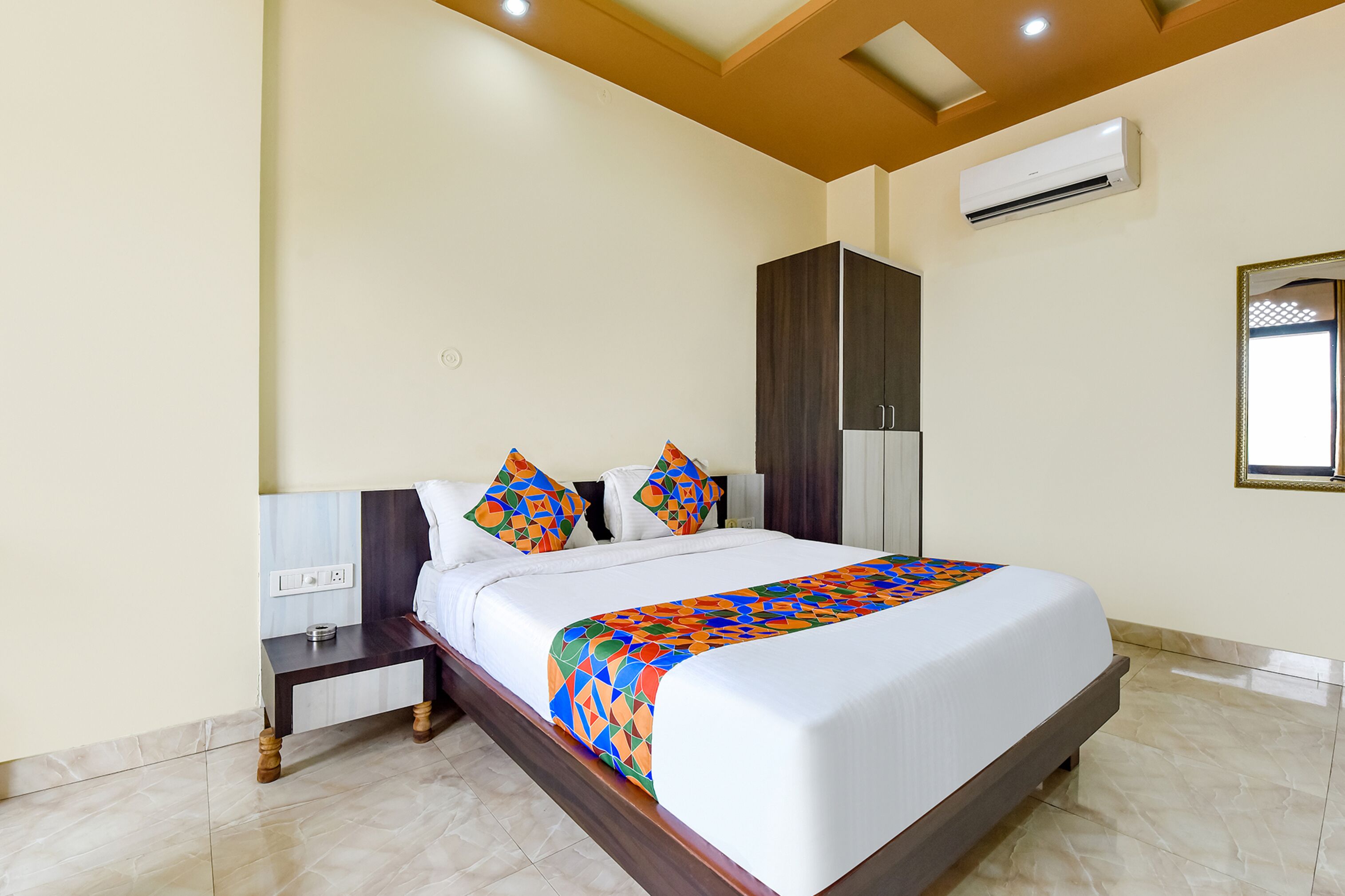 A hotel room with a large bed, a wardrobe, a nightstand, and an air conditioning unit.