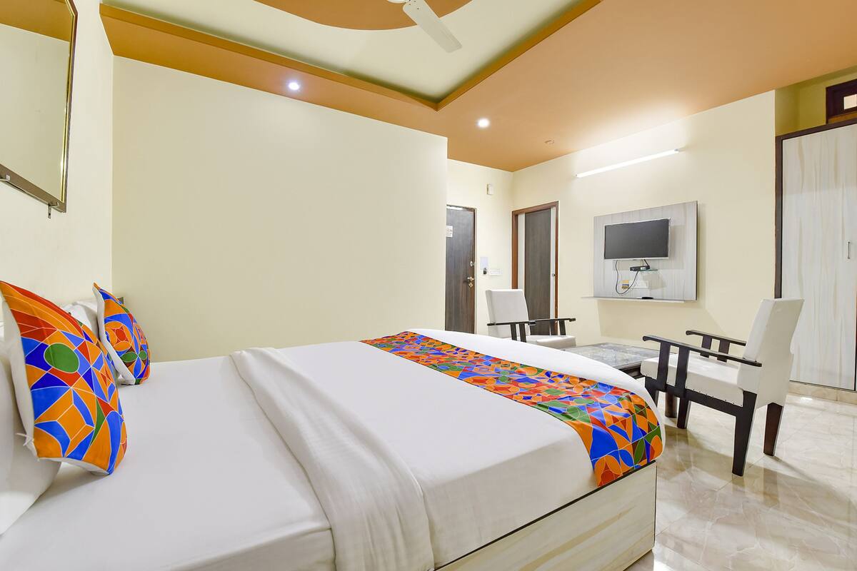 A hotel room with a bed, a desk with a chair, a TV mounted on the wall, and a wardrobe.