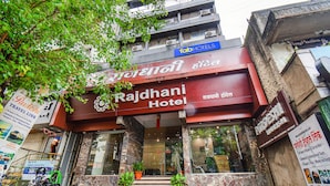 O Hotel Rajdhani com uma placa de destaque, degraus de mármore e plantas em vasos na entrada.