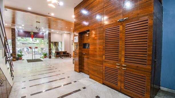 Um lobby moderno com um balcão de atendimento em madeira, porta de entrada de vidro e piso ladrilhado.