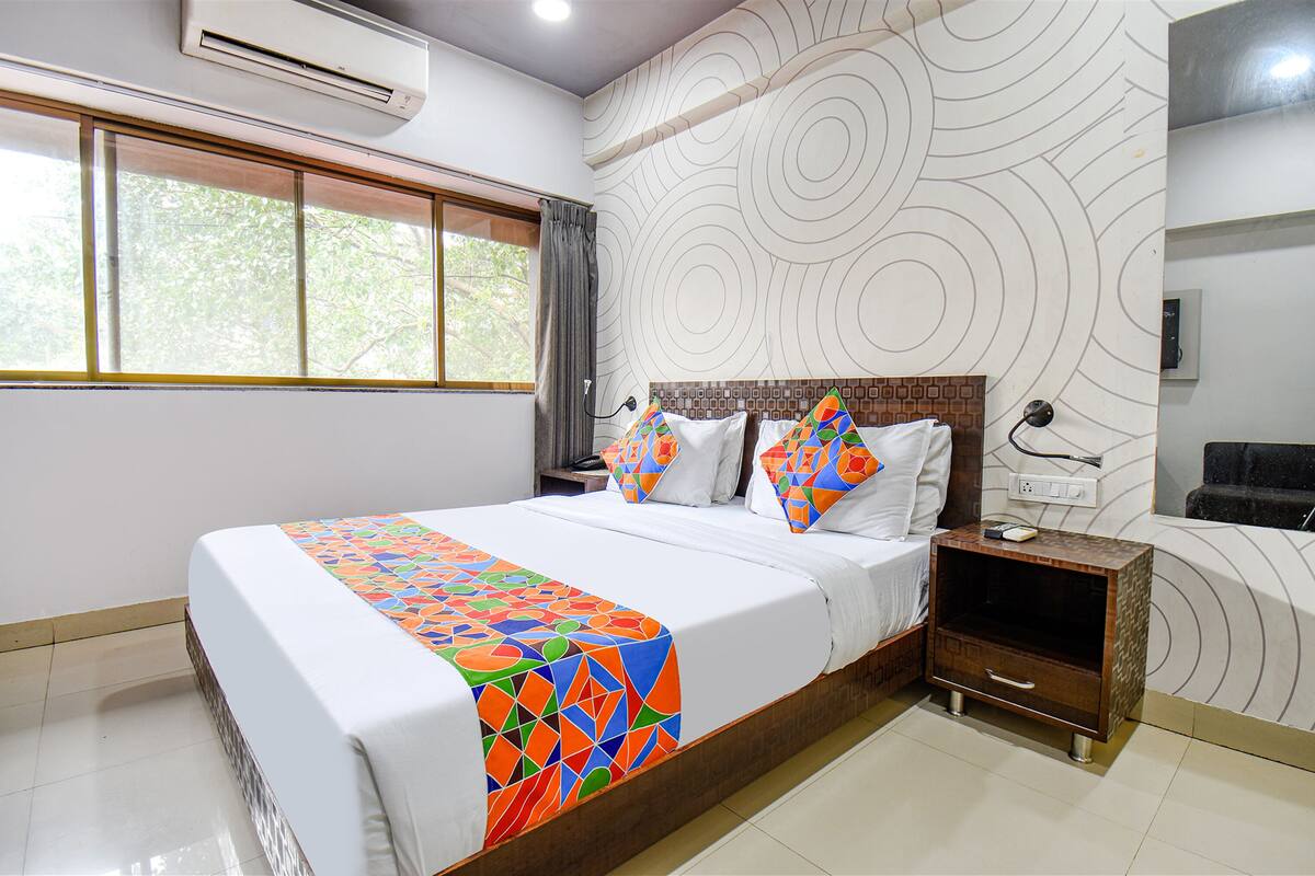 Una habitación de hotel con una cama grande, una mesita de noche, aire acondicionado instalado en la pared y una ventana con cortinas.