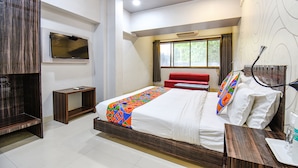 Quarto de hotel moderno com uma cama grande, televisão montada na parede, janela com cortinas e ventoinha no teto.