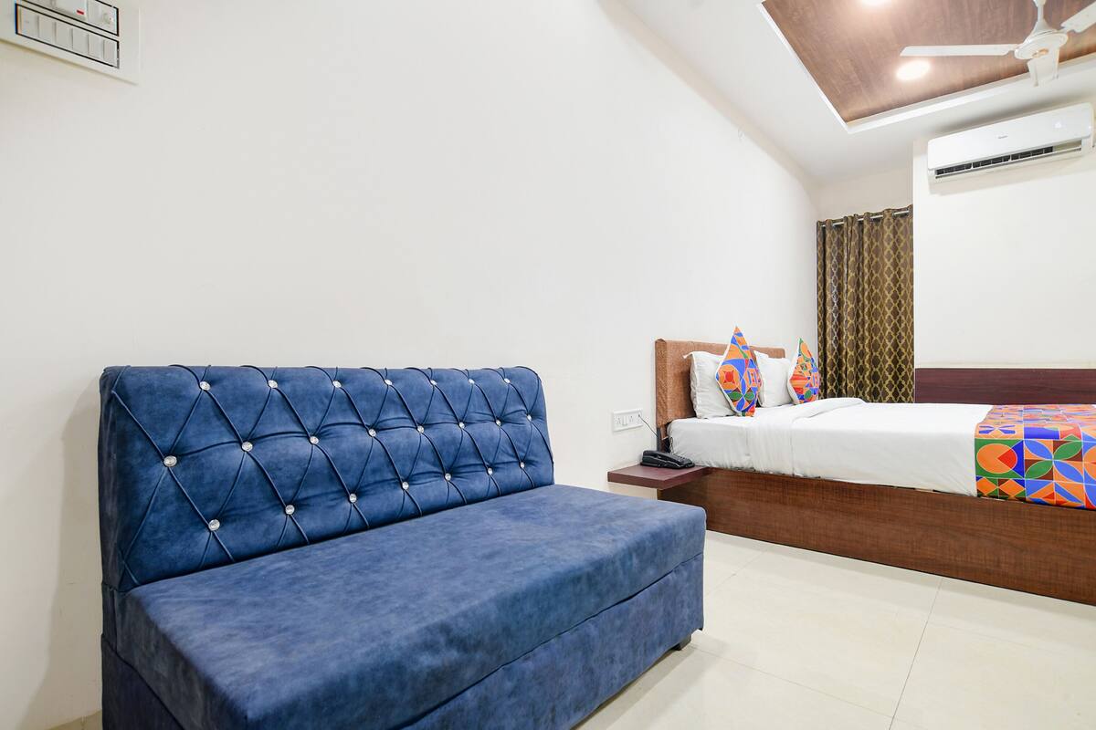 Un dormitorio con un sofá azul, una cama con ropa de cama colorida, una mesita de noche y un ventilador de techo.