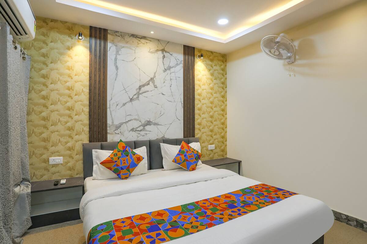 A hotel room with a bed, a nightstand, a wall-mounted fan, and a patterned wall.
